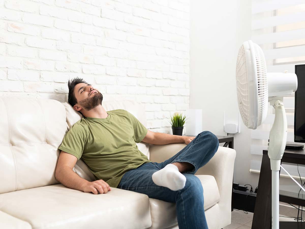 man sits in front of fan to keep cool - Air Conditioning Repair and Installation In Bardstown, KY | Above All Mechanical