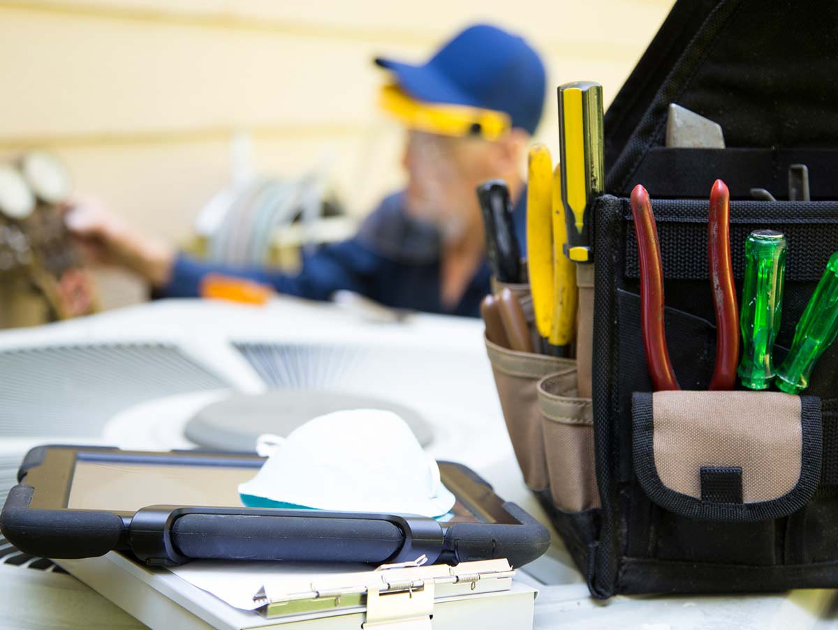 tech works on hvac system with tool bag in focus - Air Conditioning Repair and Installation In Bardstown, KY | Above All Mechanical