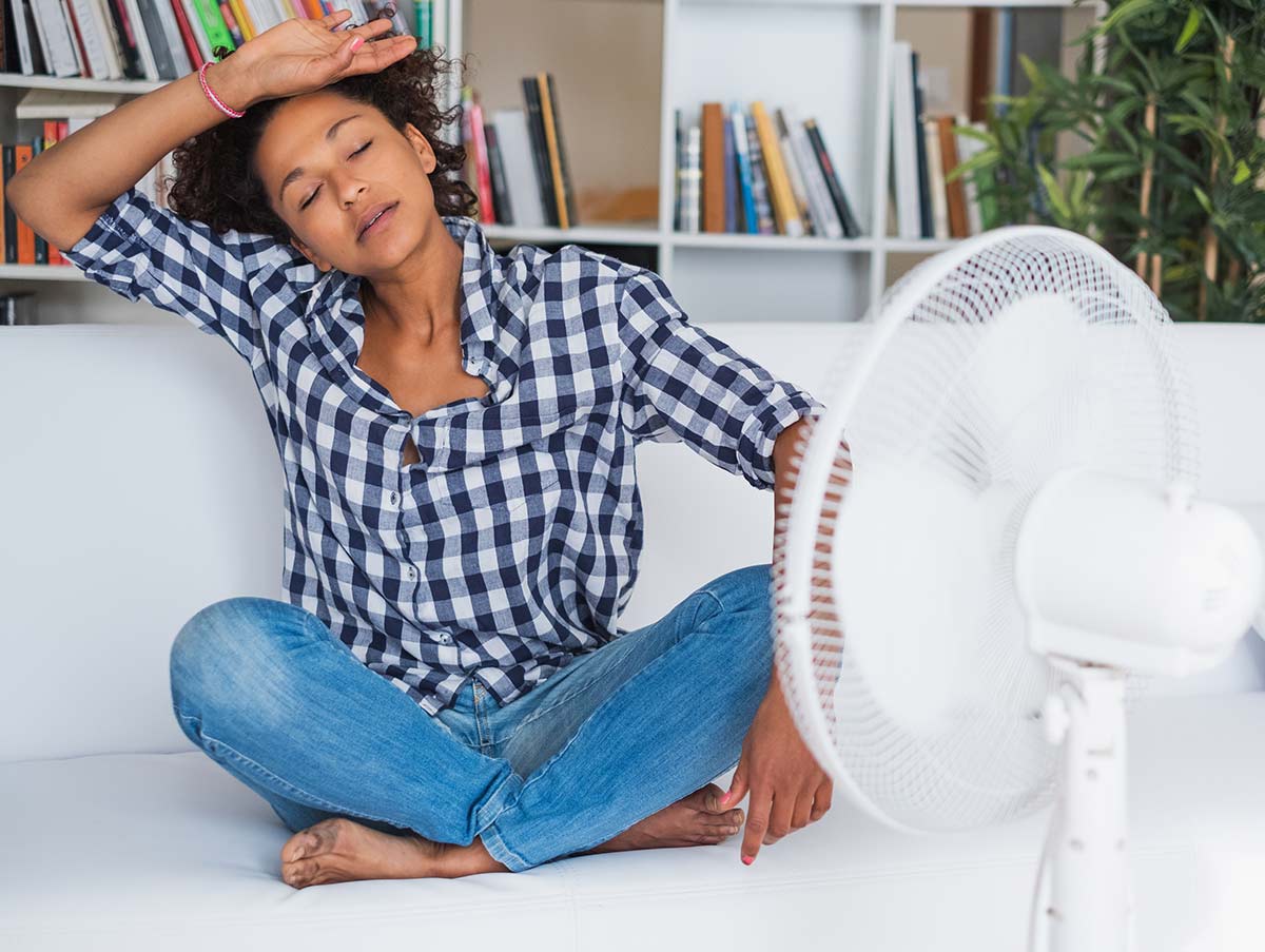 woman feeling hot in apartment uses fan to stay cool - Air Conditioning Repair and Installation In Bardstown, KY | Above All Mechanical
